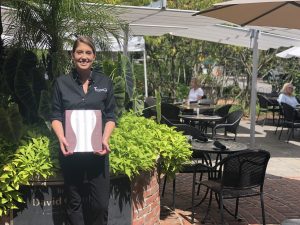 Employees outside holding menu, smiling in front of patio