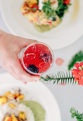 Hand holding a cocktail in a glass over a table of plated food dishes