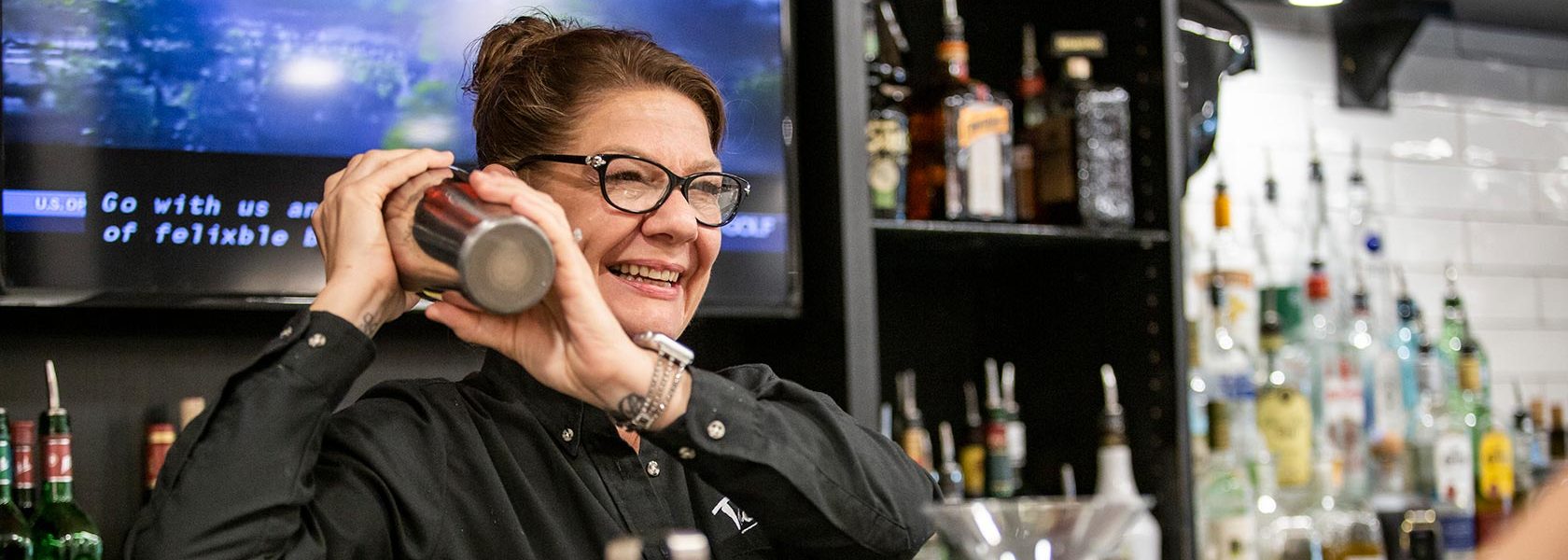 Bar chef shaking cocktail shaker over her shoulder