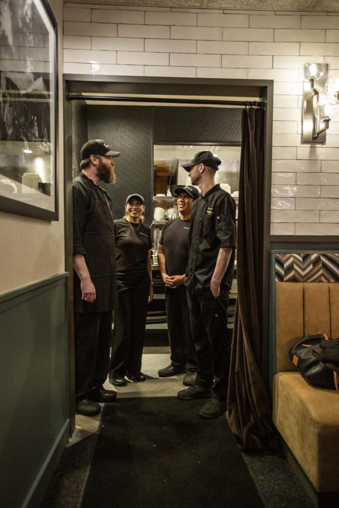 Executive chef and kitchen team standing in kitchen doorway talking.