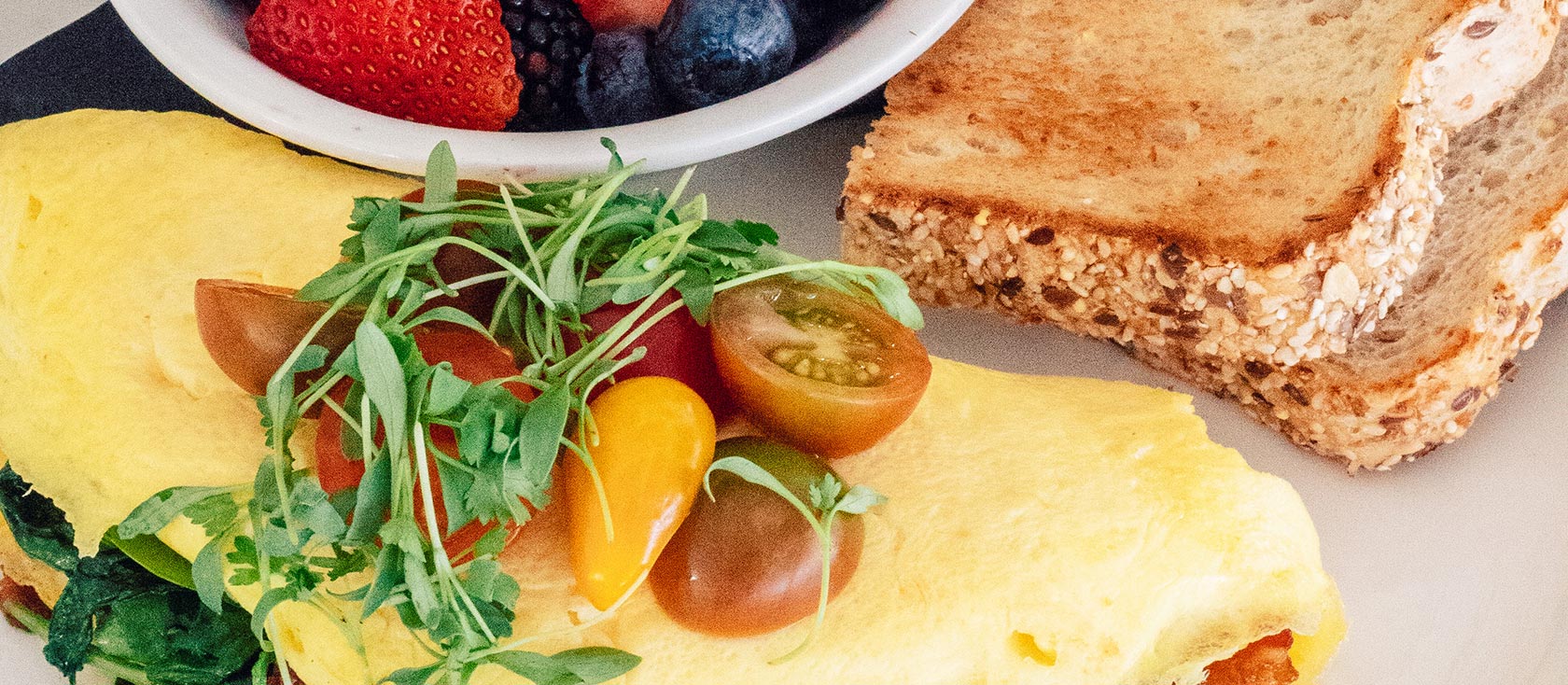 Omelet garnished with tomatoes with bowl of berries and toast