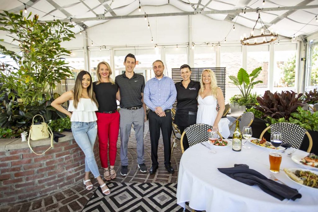 Group of six people, guests and staff, standing together in three-season covered patio.