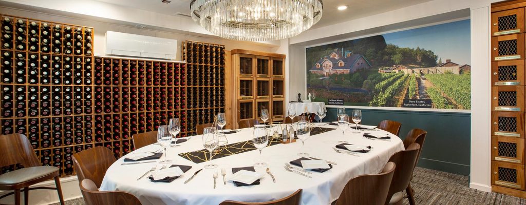 Private dining room lined with wine racks and wine lockers, table set for service for 12.