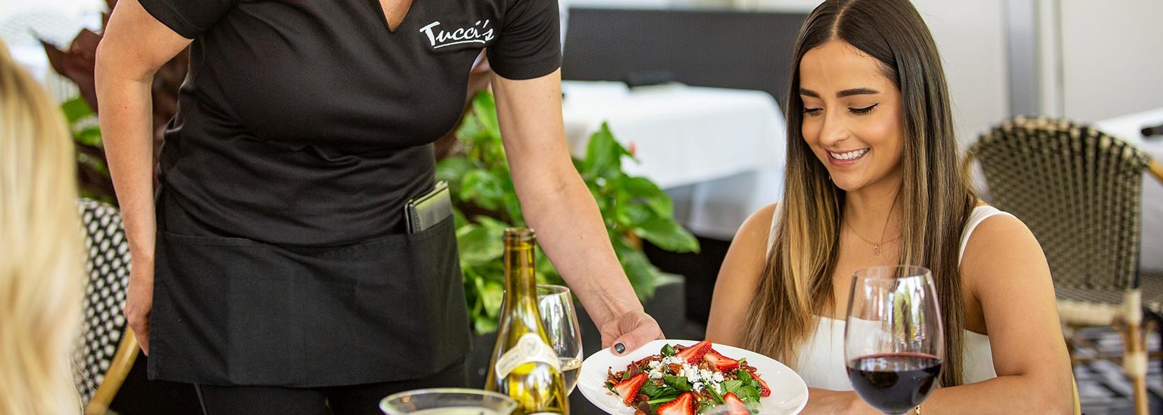 Woman being served a salad in light outdoor seating area.