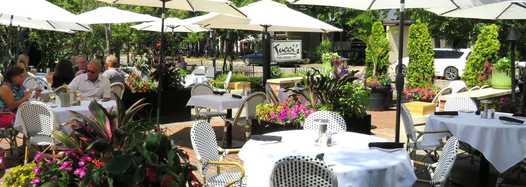 Patio dining at Tucci's in Dublin, Ohio - white umbrellas and lush foliage surround guests.