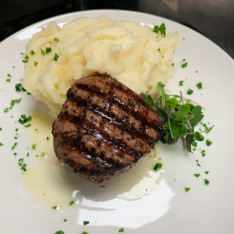 Filet steak with grilled marks plated with mashed potatoes.