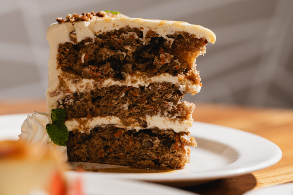 A tall slice of three-layer carrot cake with cream cheese frosting and chopped pecans on top