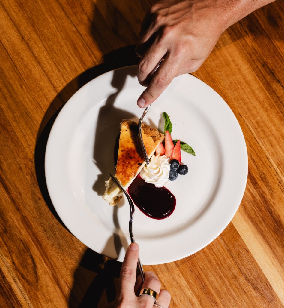 Overhead view of a slice of vanilla brulee cheesecake being cut with a knife and fork, with berries and berry sauce