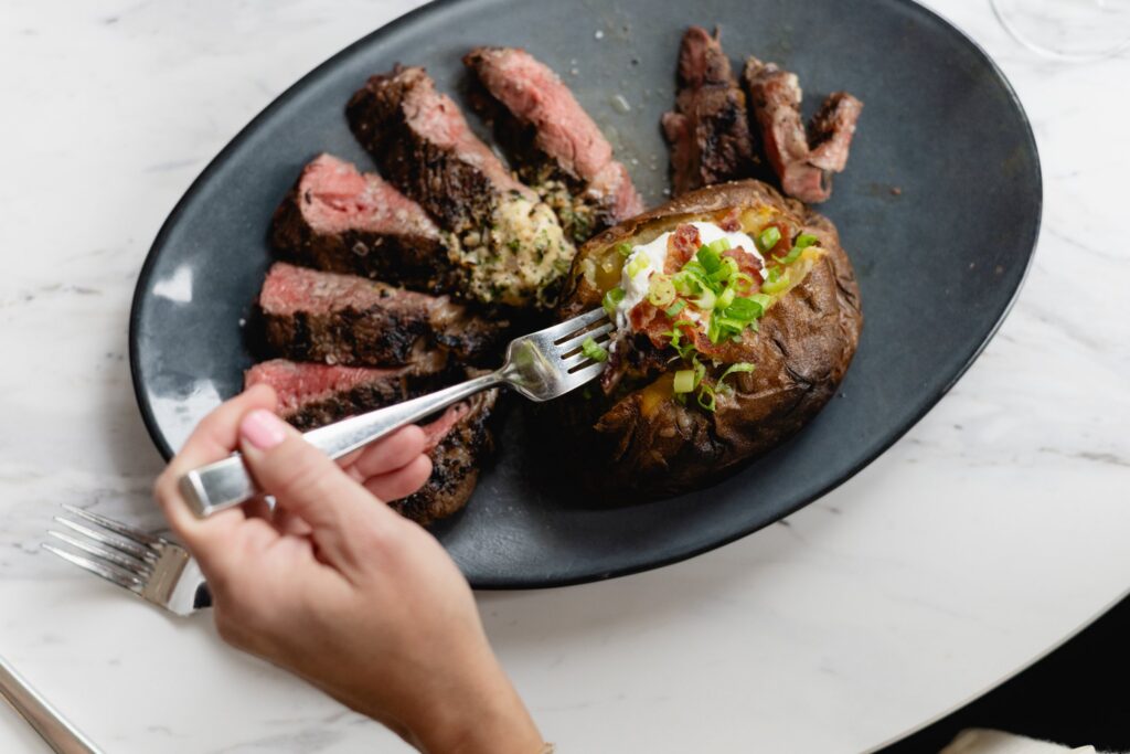 Sliced steak with compound butter and a loaded baked potato at Tucci's