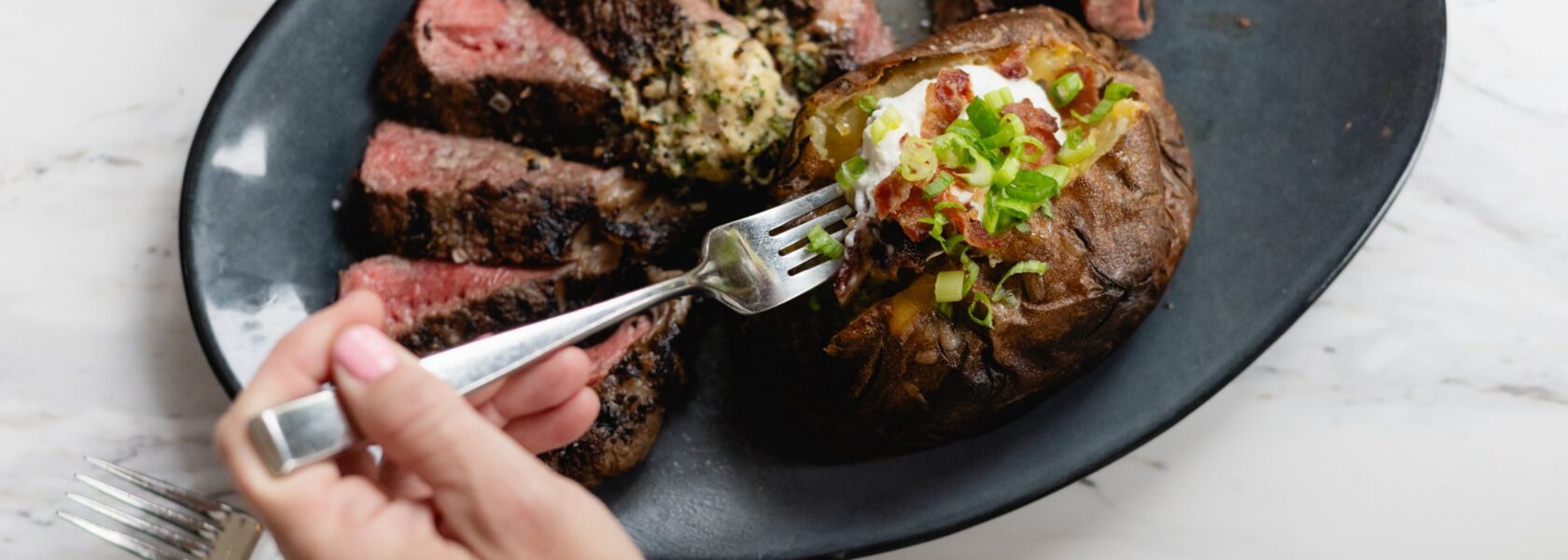 Sliced steak with compound butter and a loaded baked potato at Tucci's