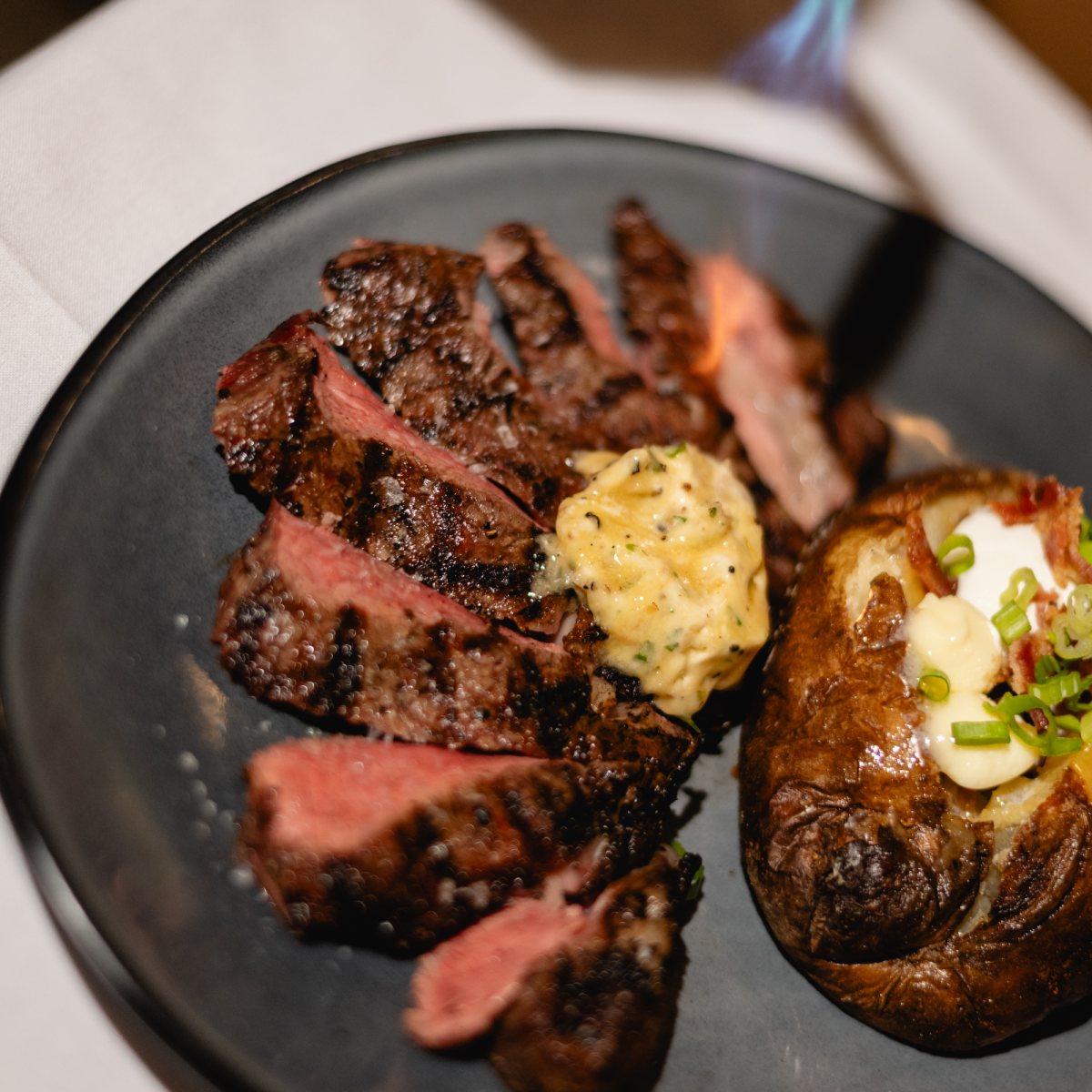 Sliced steak with compound butter and a baked potato at Tucci's